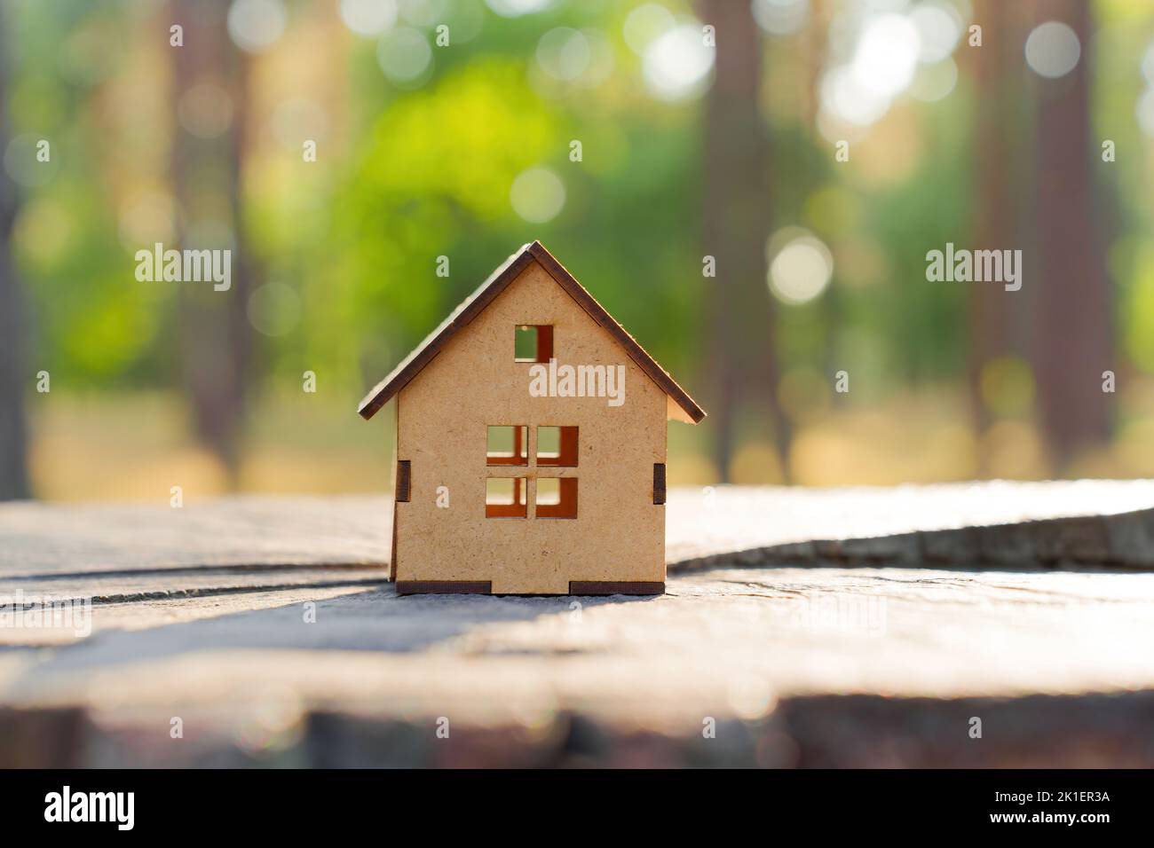 Close-up of a wooden toy house model placed on a tree stump in a forest area. Nature and real estate concept. Stock Photo