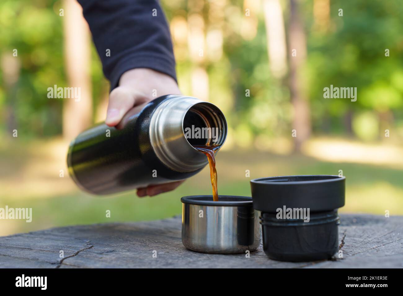 Hikers having a coffee break in the woods. Pouring coffee from a vacuum bottle using a large tree stump as a table. Stock Photo
