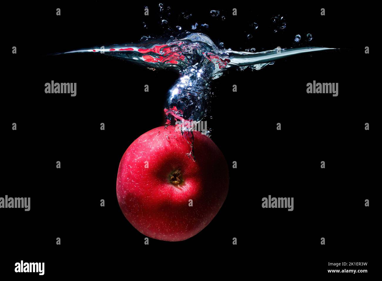 Red apple sinking in water with splashes isolated on black background
