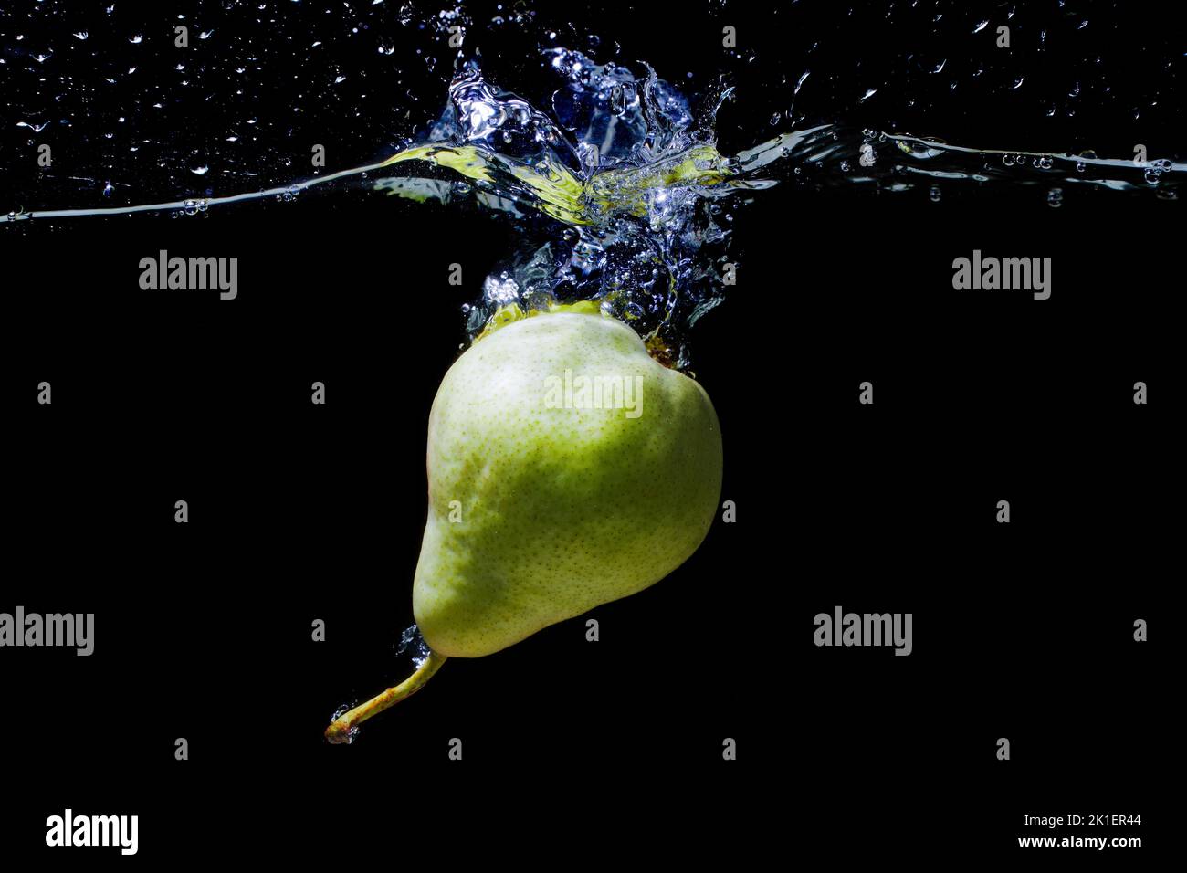 Whole green pear dropped in water with splashes isolated on black background. Stock Photo