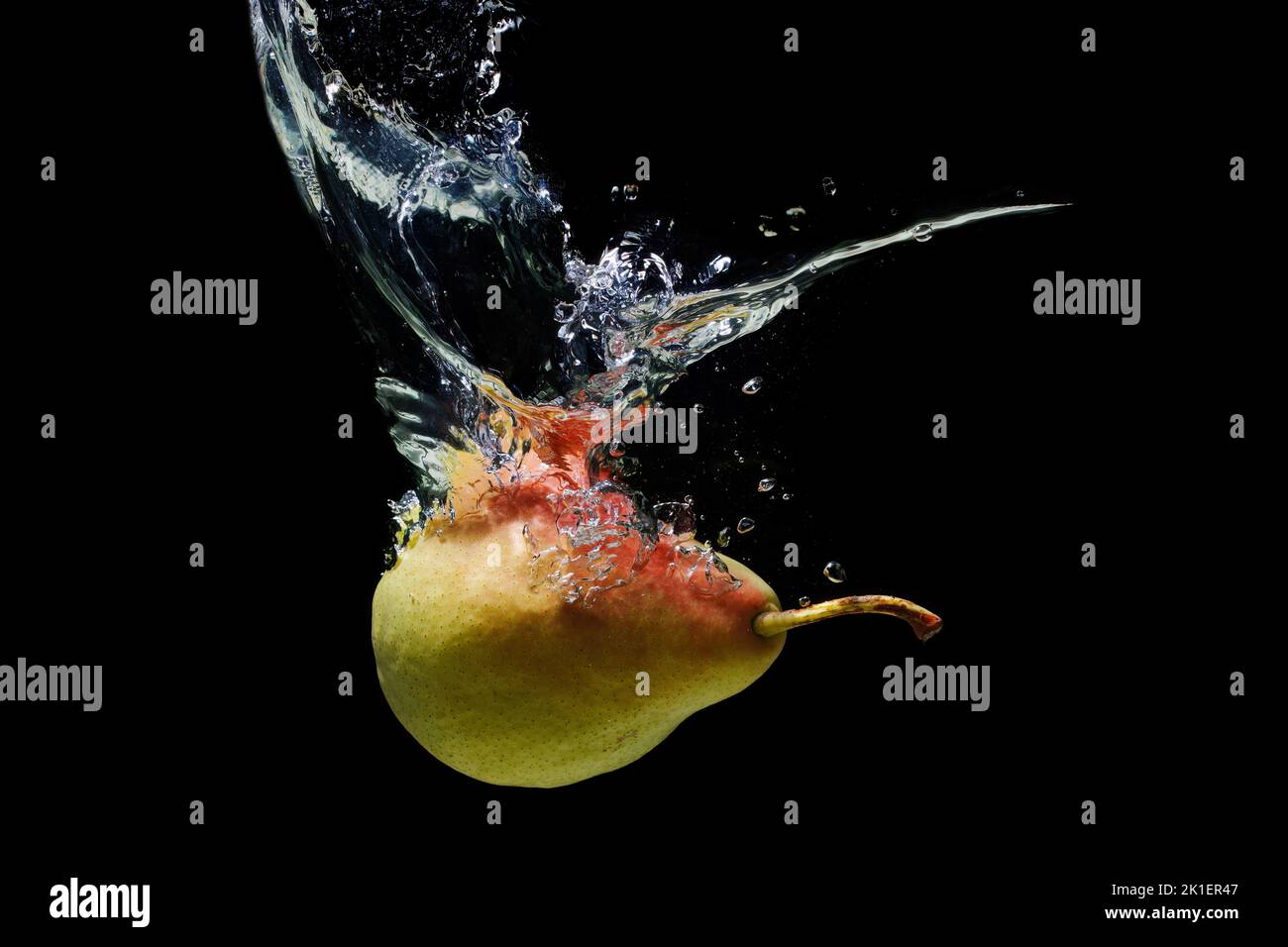 Ripe whole pear falling underwater with splashes isolated on black background. Stock Photo
