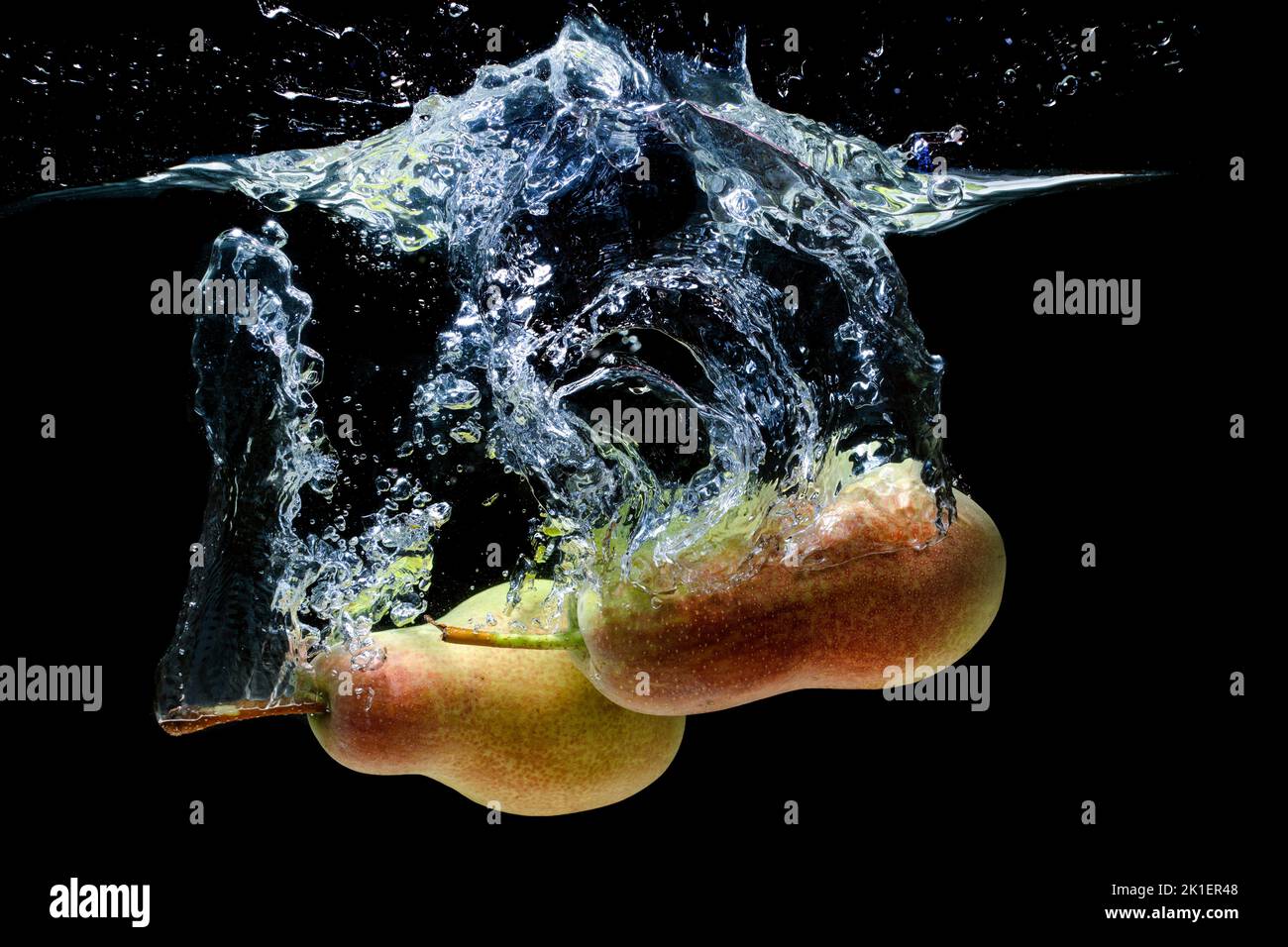 Close-up of two ripe whole pears dropped in water with splashes isolated on black background. Stock Photo