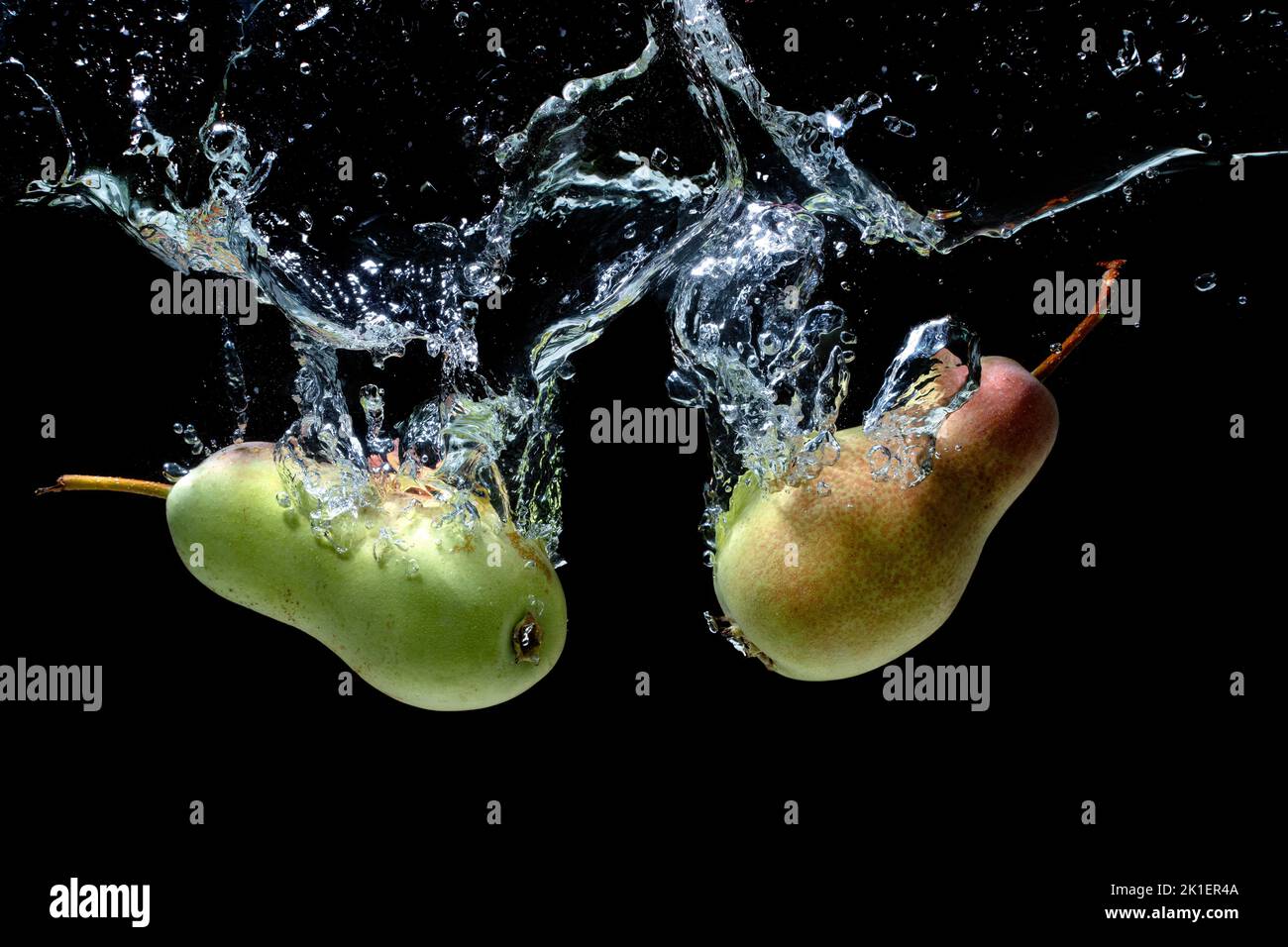 Two fresh pears falling underwater with splashes isolated on black background. Stock Photo