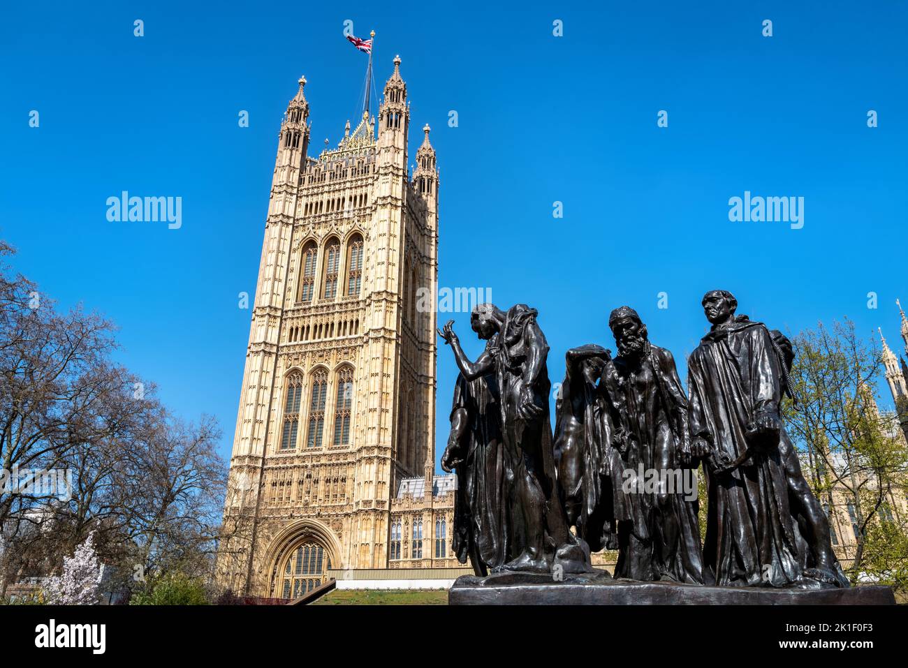 The Burghers of Calais statue, by Auguste Rodin, completed in 1889, outside of the Houses of Parliament, London, UK. The Victoria Tower has a Union Ja Stock Photo