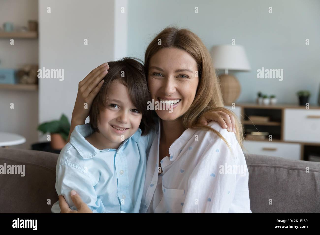 Cheerful loving mother and little son kid hugging on couch Stock Photo