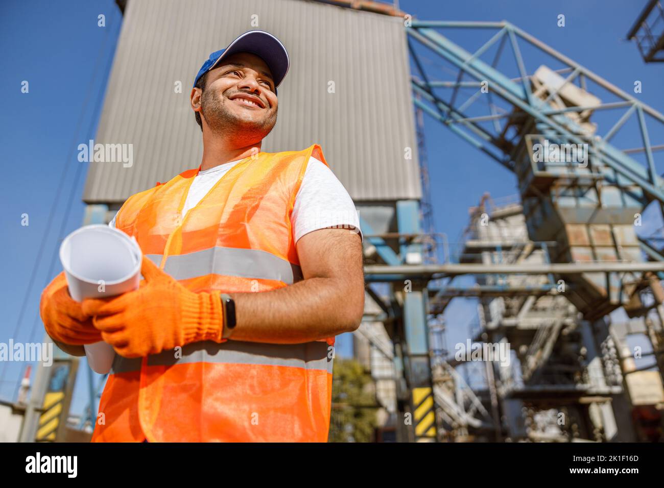 Happy construction engineer working on blueprint at plant Stock Photo