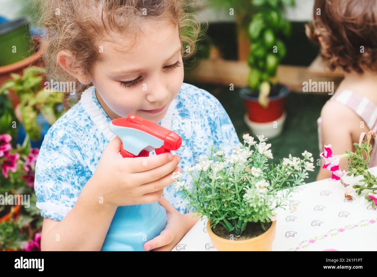 A cute young girl watering a house plant with white flowers using a