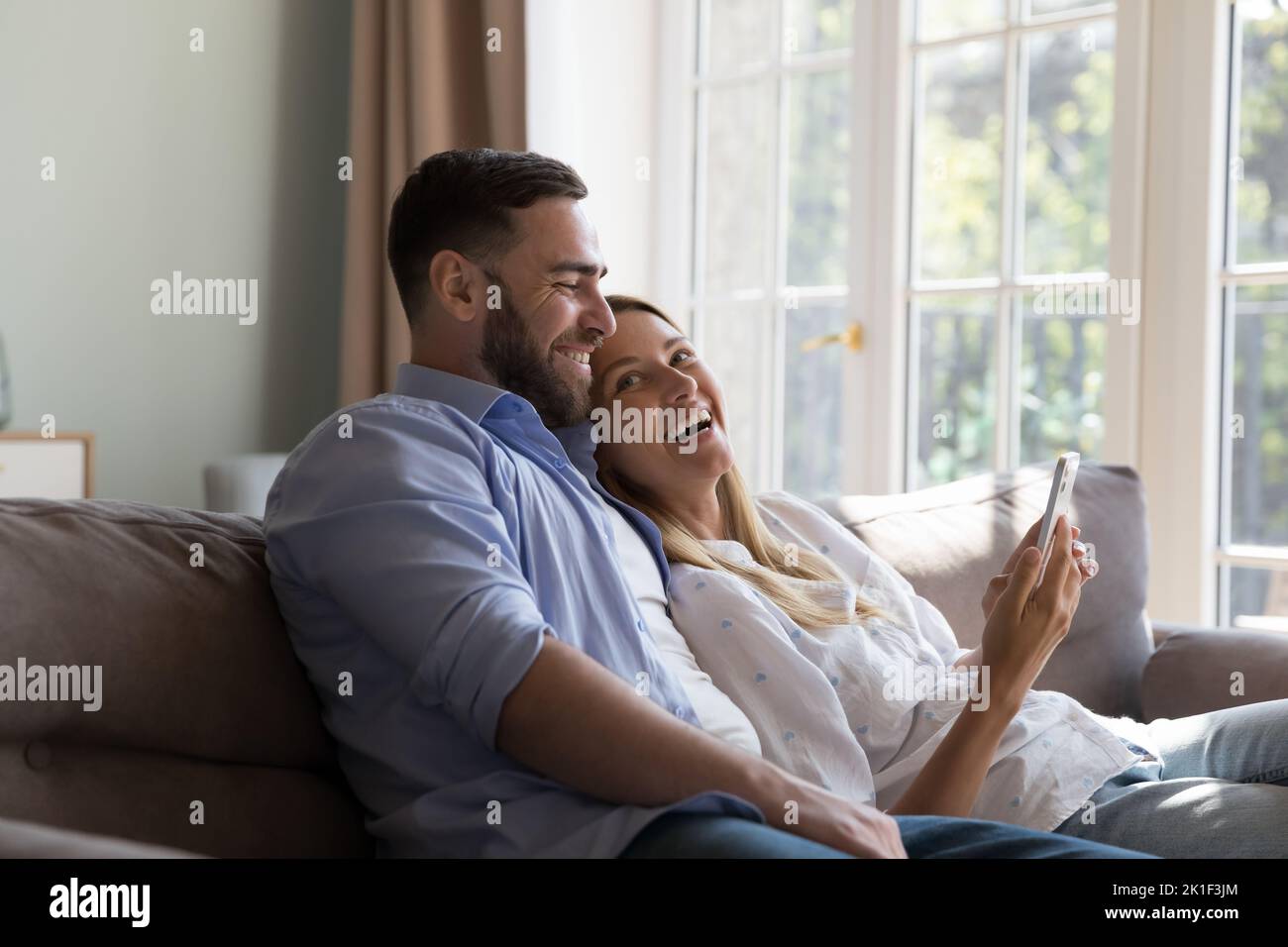 Happy cheerful married couple relaxing, hugging on couch at home Stock Photo