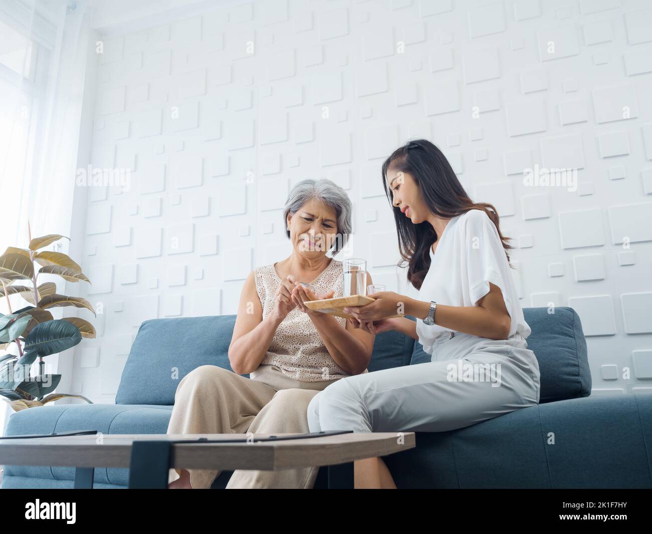 Portrait of Asian senior woman grey short hair holds pill and a glass of drinking water from young adult daughter, taken daily medicine or vitamin sup Stock Photo