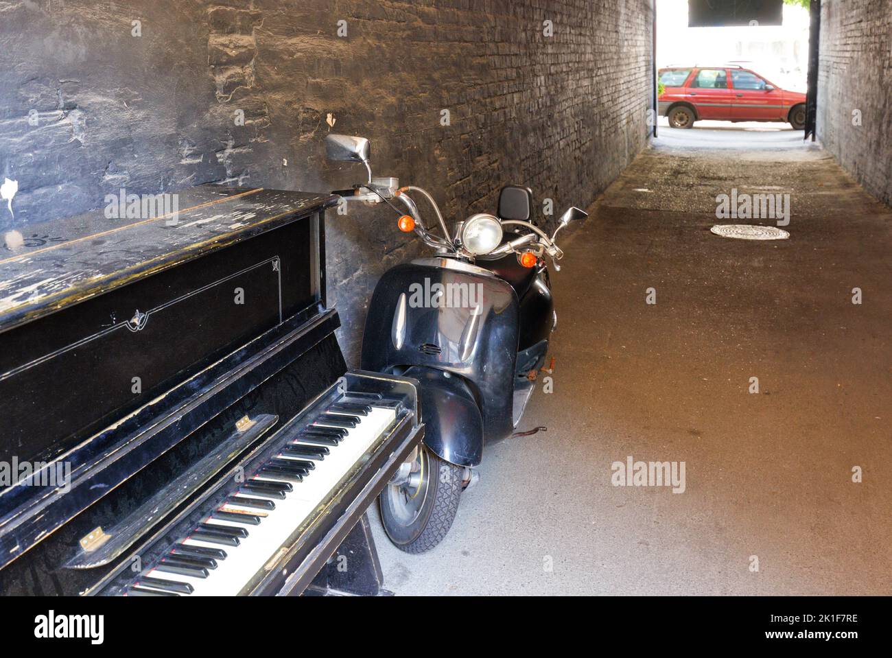 A vintage black piano with a retro black moped in the archway of a house on a sunny day. Copy space. Stock Photo