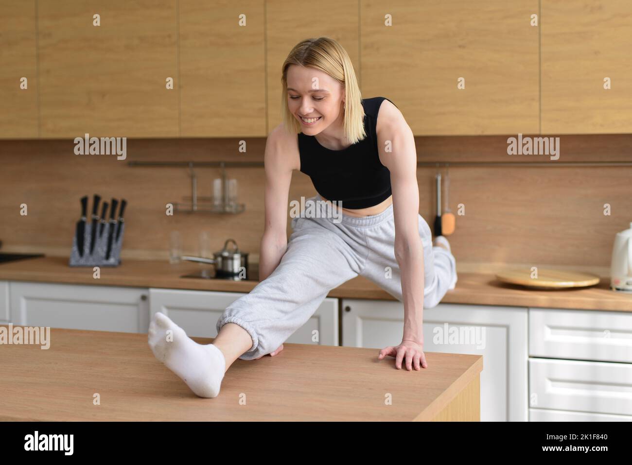 Woman doing the splits in kitchen between tables. Stock Photo