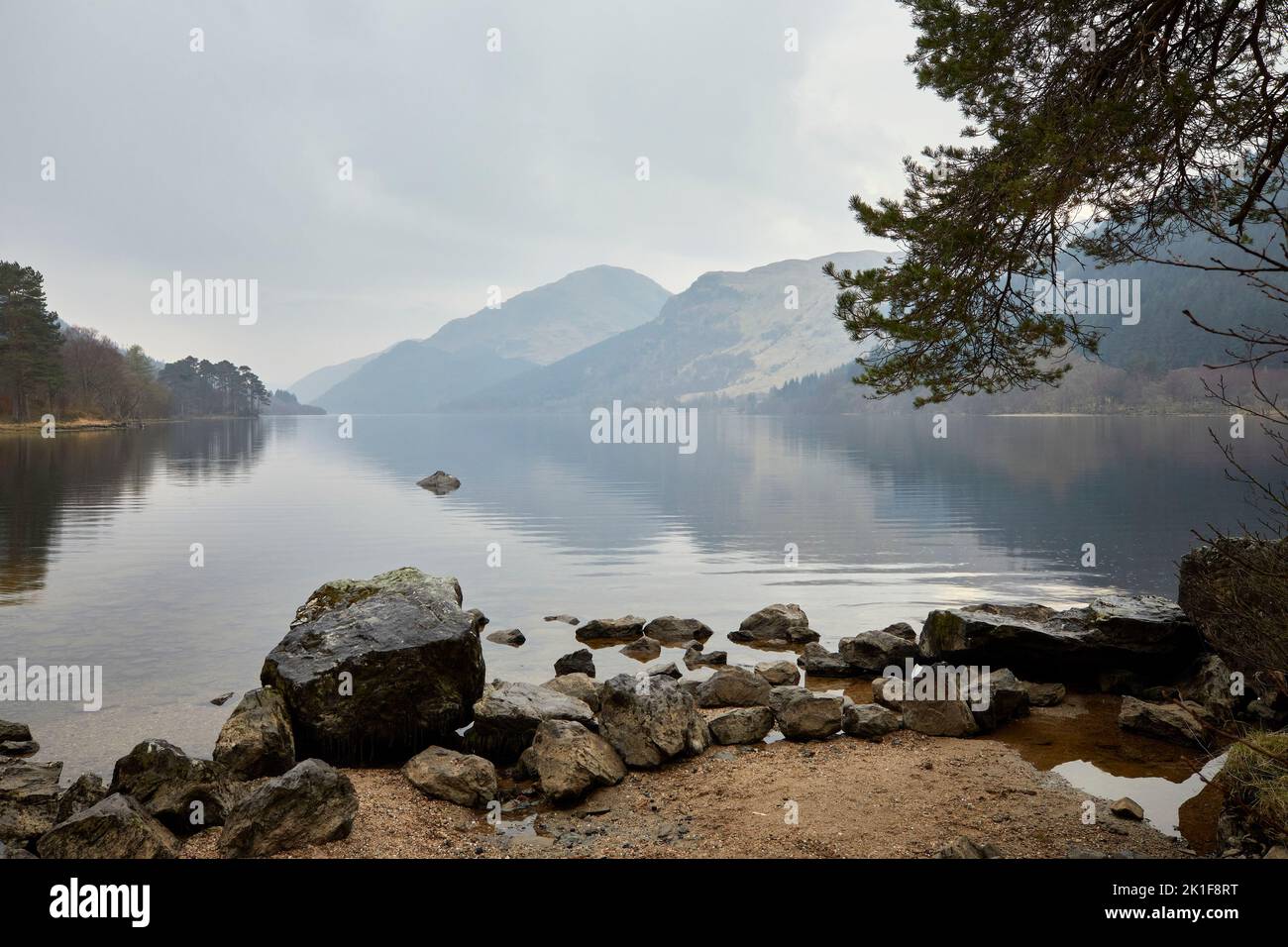 Looking south from Jubilee Point, on a late March evening, gentle rain begins to fall on the reflective still surface of Loch Eck. Argyll and Bute Stock Photo