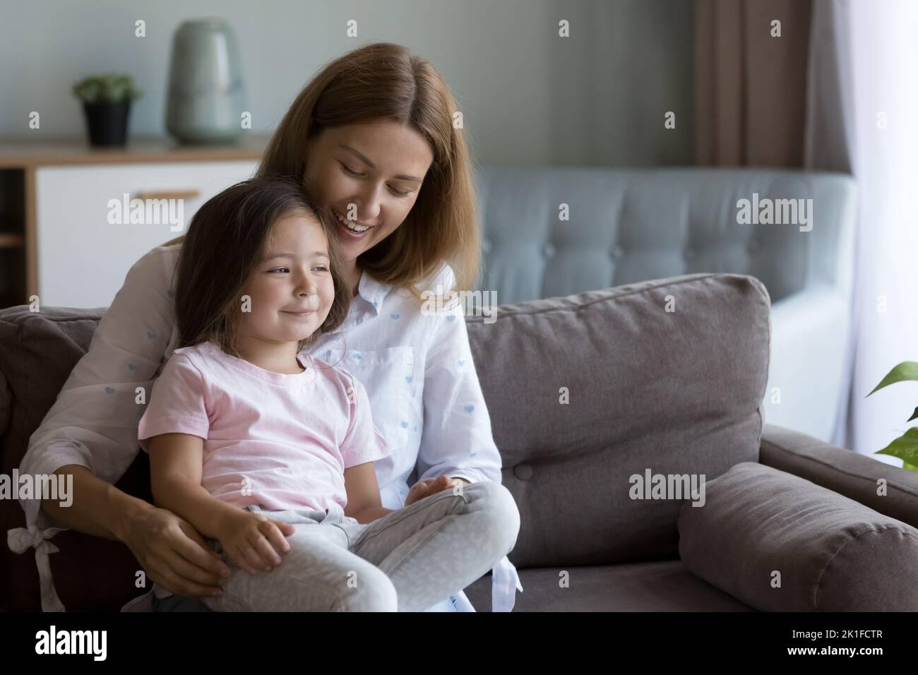 Cheerful mom holding happy daughter in arms on sofa Stock Photo