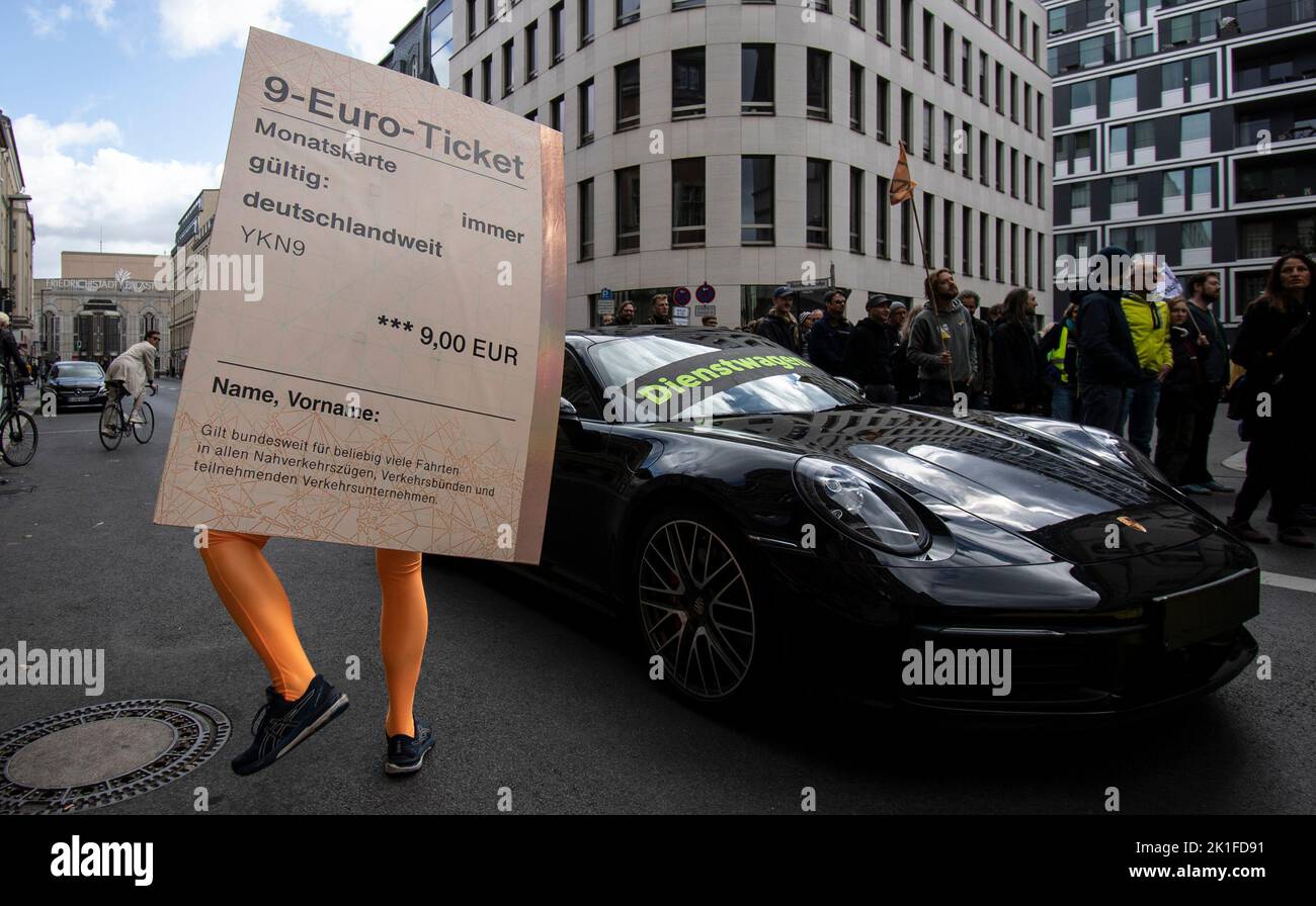 18 September 2022, Berlin: "Company car" is written on a Porsche 911 while  a demonstrator with an oversized "9-Euro-Ticket" stands next to it during a  protest action of the environmental protection organization