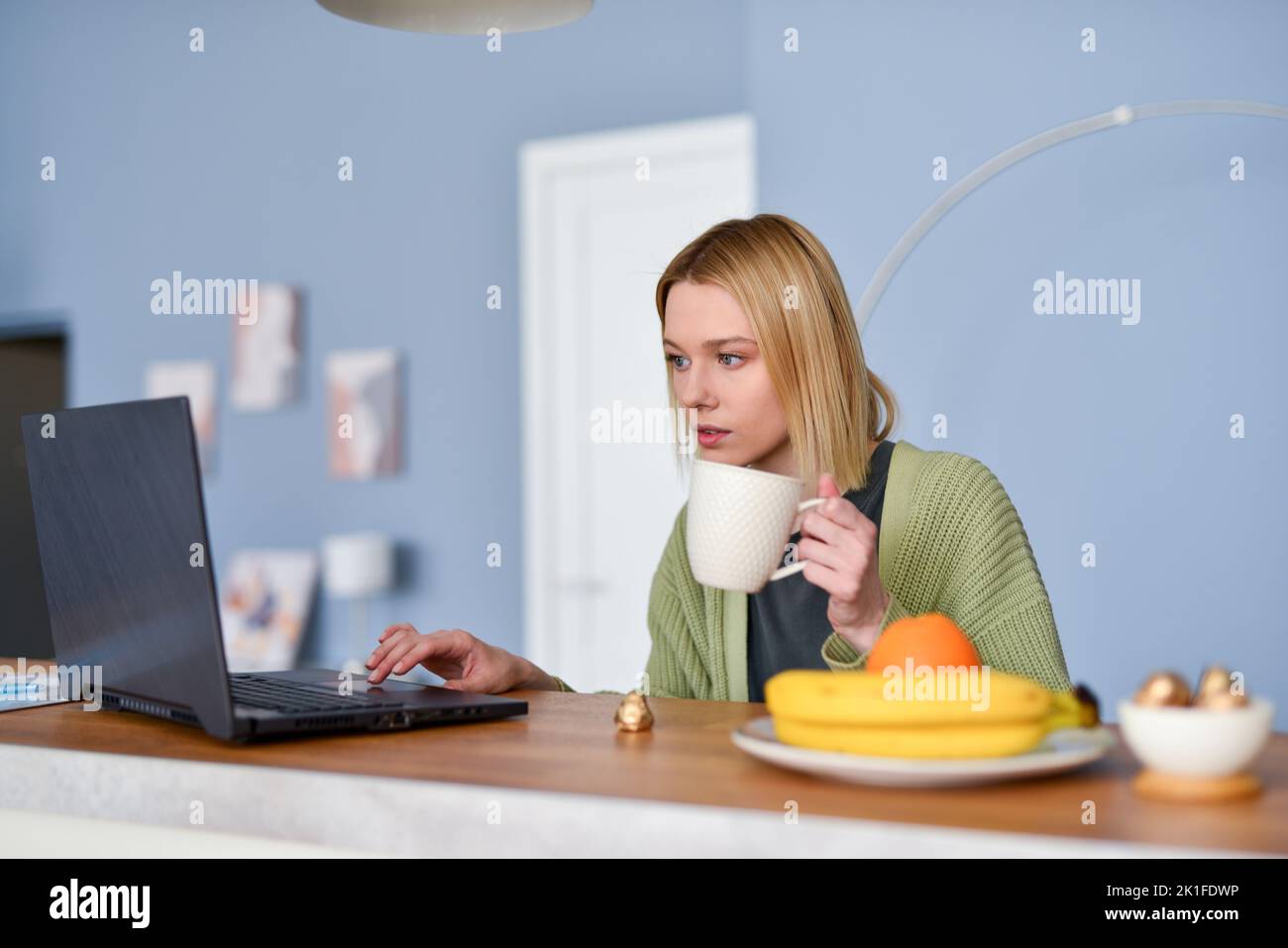 Young woman having breakfast or lunch at home with her laptop in the kitchen. Stock Photo