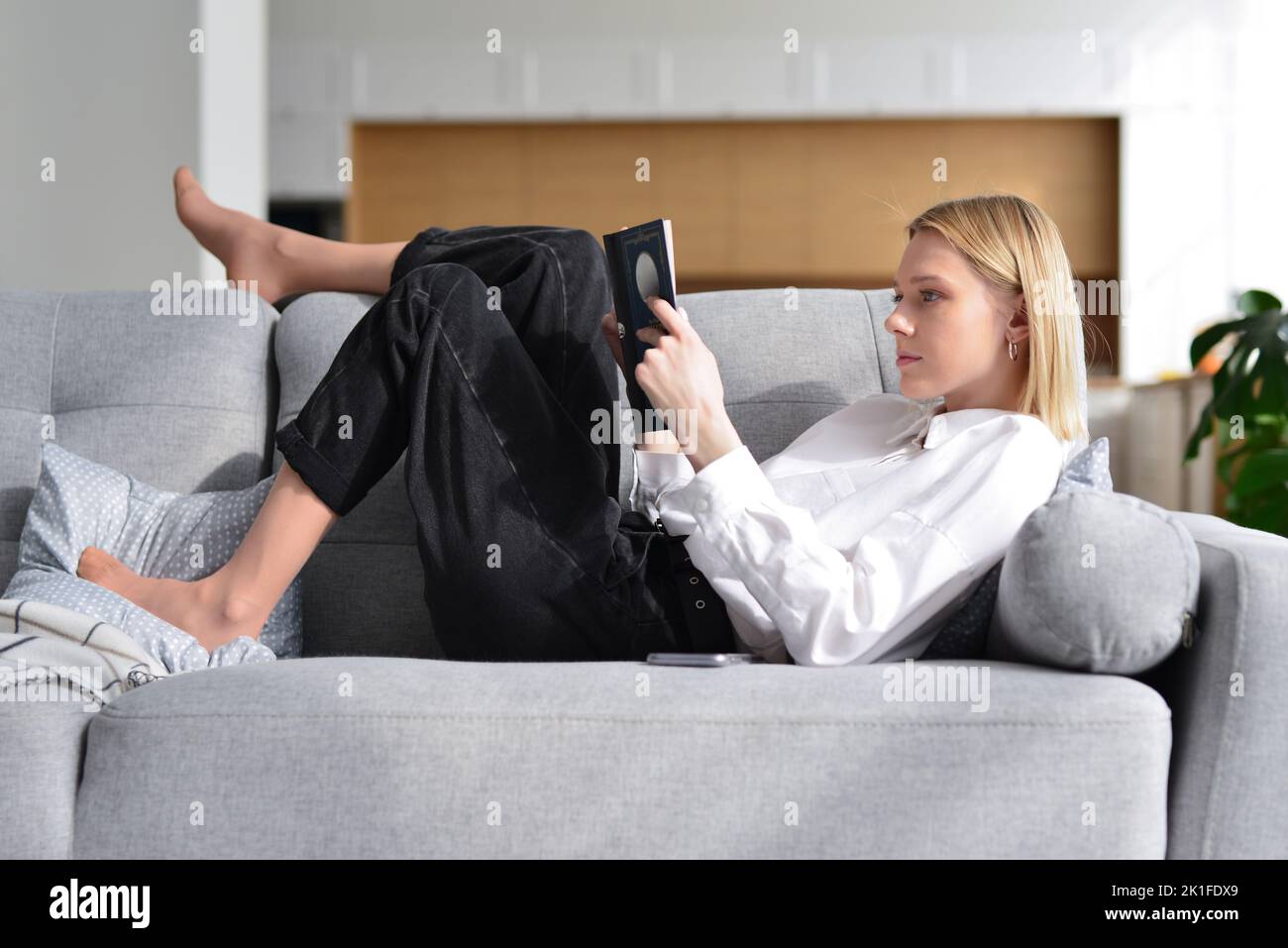 Woman lies on sofa and reads book. Stock Photo