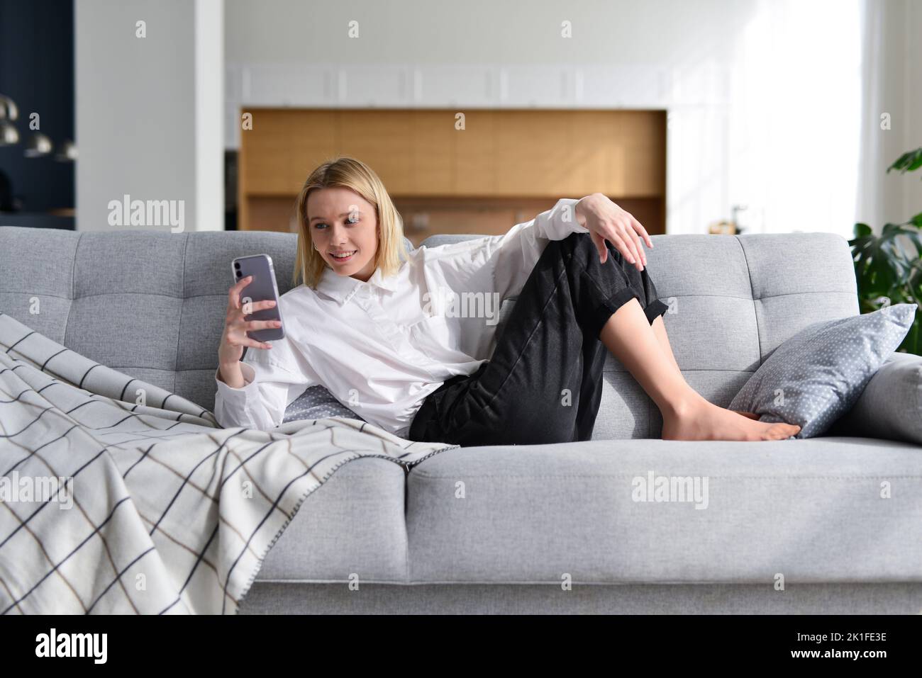 Woman with smartphone at home lying on sofa. Stock Photo