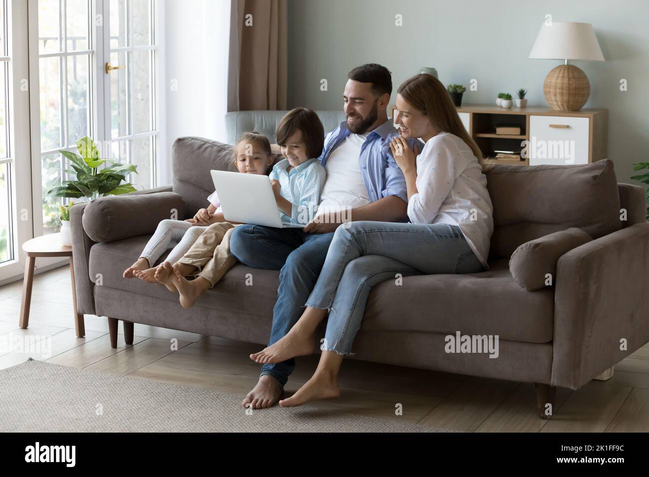 Happy parents and two little gen Z resting on sofa Stock Photo
