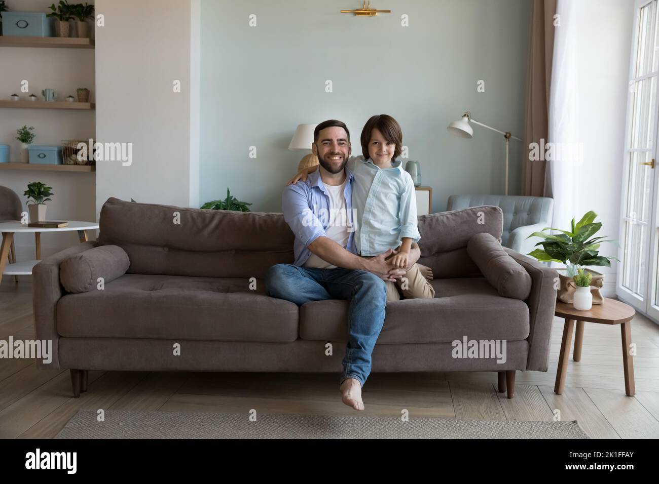 Happy handsome dad and little son kid sitting on sofa Stock Photo