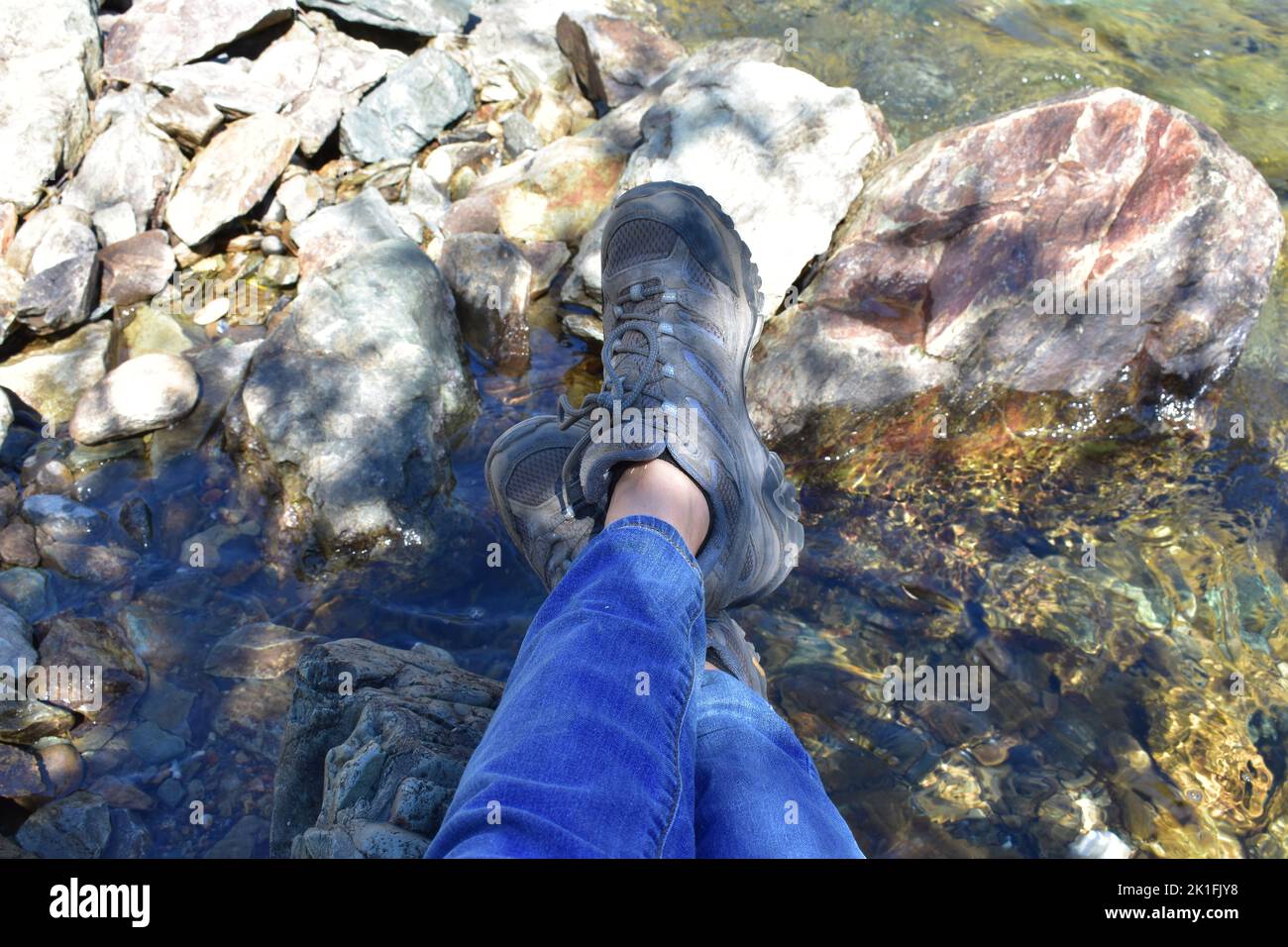 Crossed Ankles in Hiking Boots and Jeans Resting Riverside Stock Photo