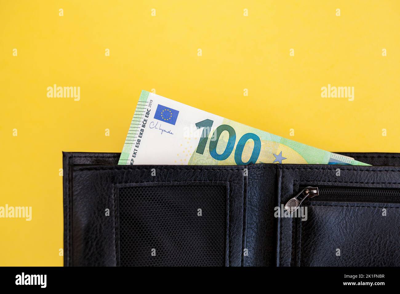 100 euro banknote sticks out of a black wallet on a yellow background Stock Photo