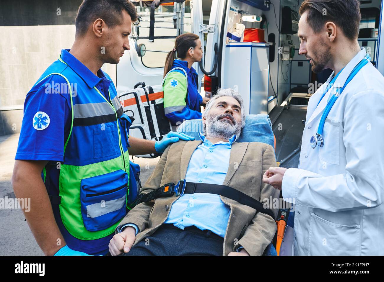 Paramedic and doctor examining of senior male patient lying in ambulance gurney brought to hospital by EMT workers. Emergency medical services and car Stock Photo