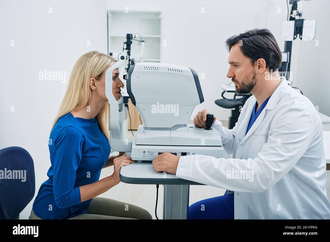 Experienced ophthalmologist man using automated refractor for vision correction female patient in ophthalmic office Stock Photo