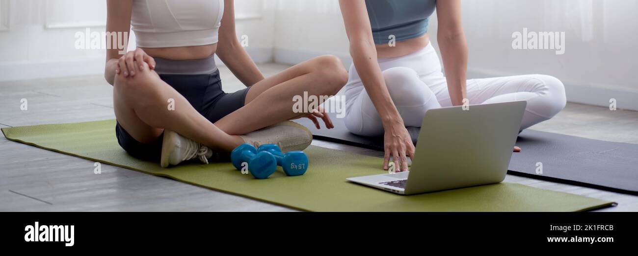 Young woman practicing exercise or yoga on mat while watching laptop computer tutorial online at home, woman having motivation looking notebook for wo Stock Photo