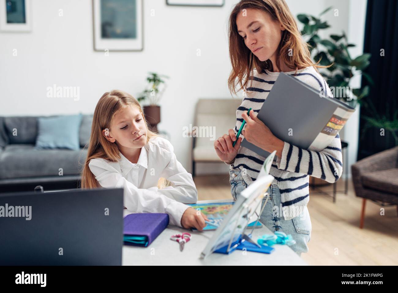 Mother standing next to her daughter doing homework. Stock Photo