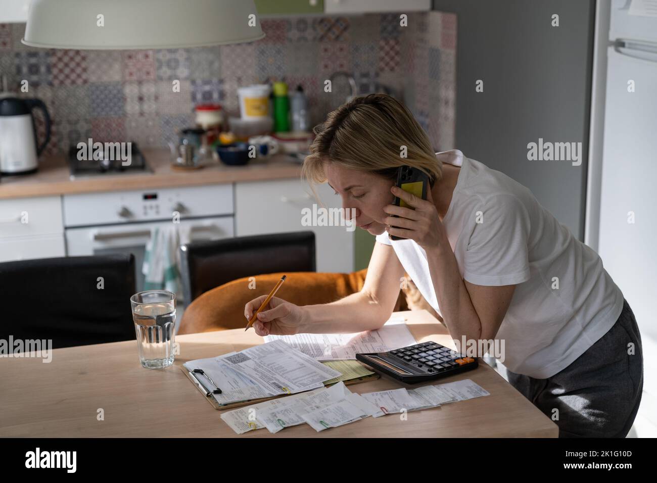 Mature woman talks on phone with hotline trying to solve problem checking unpaid bills at table Stock Photo