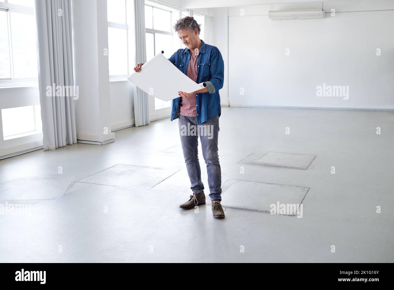 This rooms going to look great. A mature man looking at building plans while standing in an empty room. Stock Photo