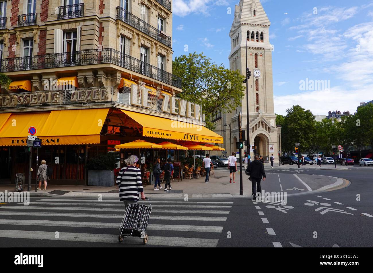 People walking in front of Brasserie Le Zeyer and Saint Pierre de Montrogue church at Alesia in the 14th arrondissement, Paris, France Stock Photo