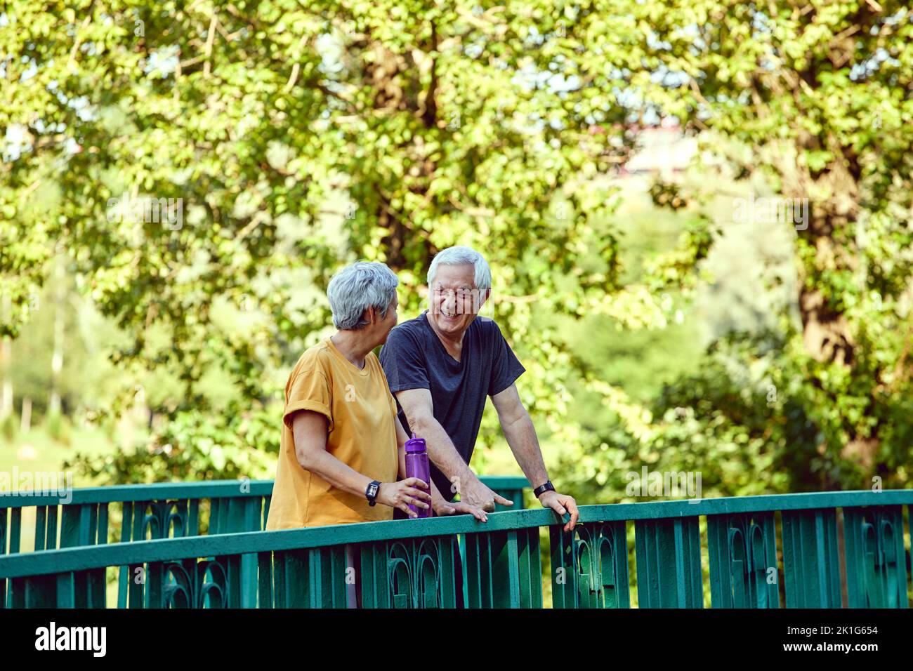 Attractive middle-aged old couple, wife and husband enjoy a walk and communication in summer park during morning sportive stroll with water. Communica Stock Photo