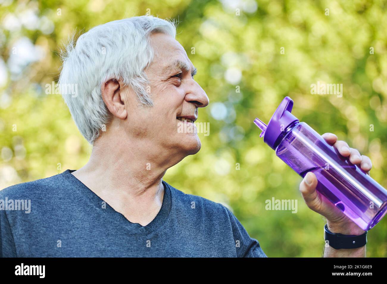 Close up image attractive mature man holds plastic reusable bottle drinking still mineral water during morning work out or stroll in summer park, cari Stock Photo