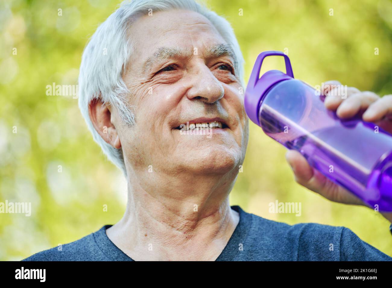 Close up image attractive mature man holds plastic reusable bottle drinking still mineral water during morning work out or stroll in summer park, cari Stock Photo