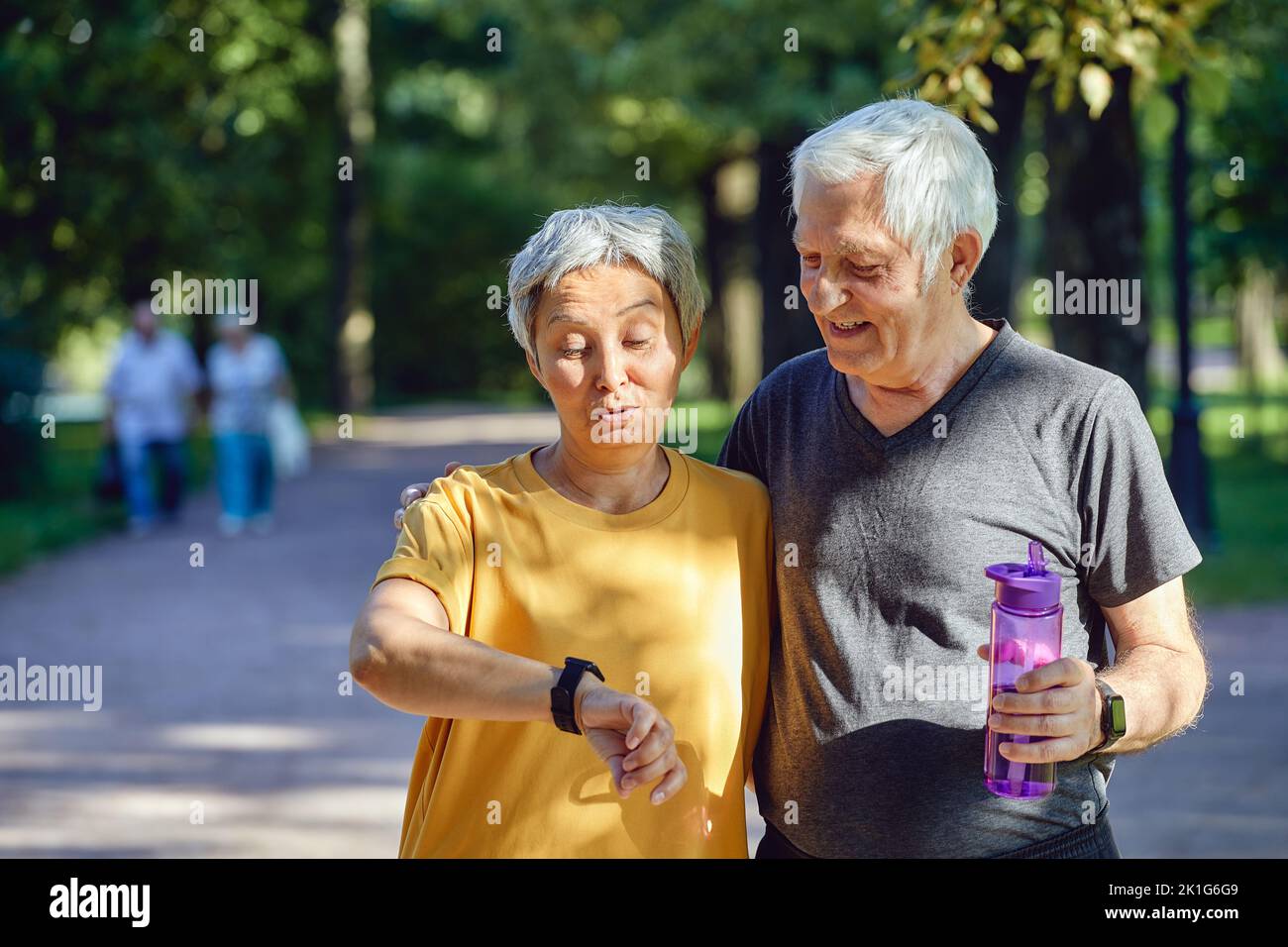 Aged couple work out in summer park wear watch check data using application caring about health. Active sporty retired spouses lifestyle using modern Stock Photo