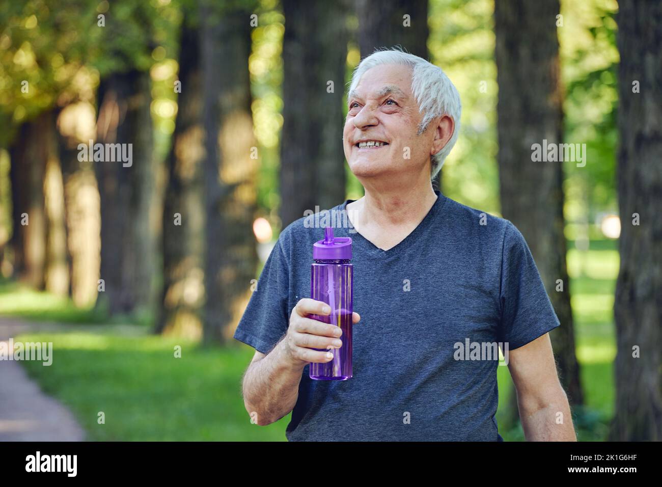 Older man in sportswear holds reusable plastic bottle standing or jogging in summer park, caring about health, enjoy morning work out feels happy. Hea Stock Photo