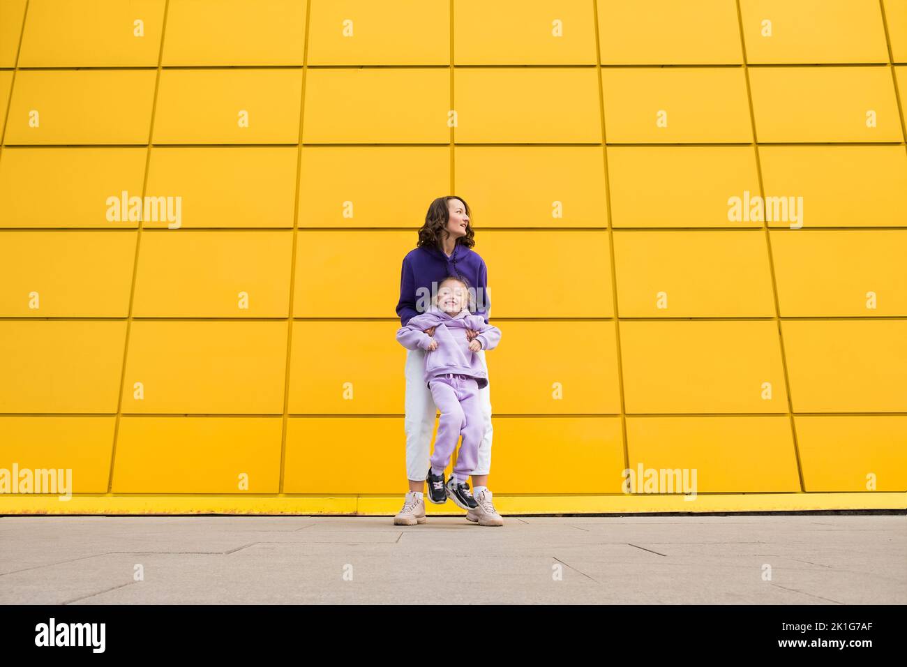 Woman in purple hoody have fun with cute girl 4-5 years old. Mommy and little daughter on yellow mall wall background. Childhood concept of love for Stock Photo