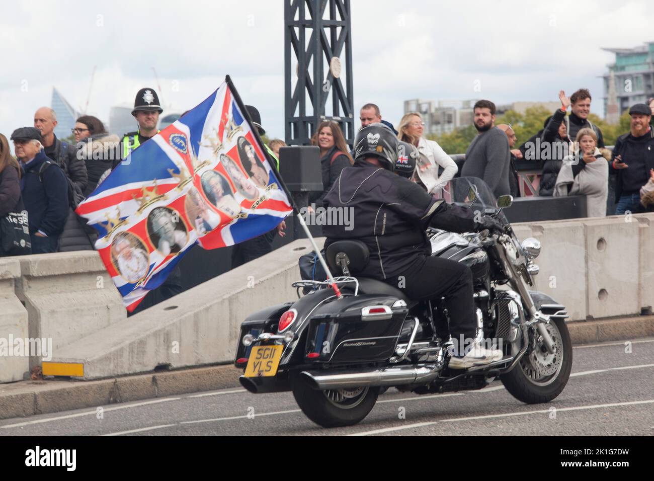London, UK, 18 September 2022: A motorbike with a flag of the late Queen drives past mourners who are queueing on Lambeth Bridge to pay their respects to the late monarch Queen Elizabeth II, whose funeral takes place tomorrow. The queue for admission to Westminster Hall has now closed in order for all of those already in the queue to pass through before 6.30am tomorrow morning. Anna Watson/Alamy Live News Stock Photo
