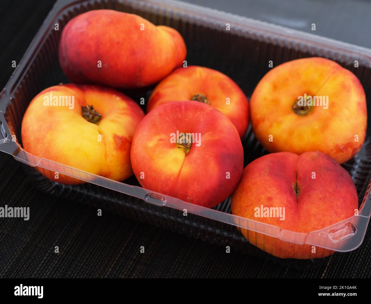 A plastic container with ripe flat peaches in it on black bamboo napkin Stock Photo