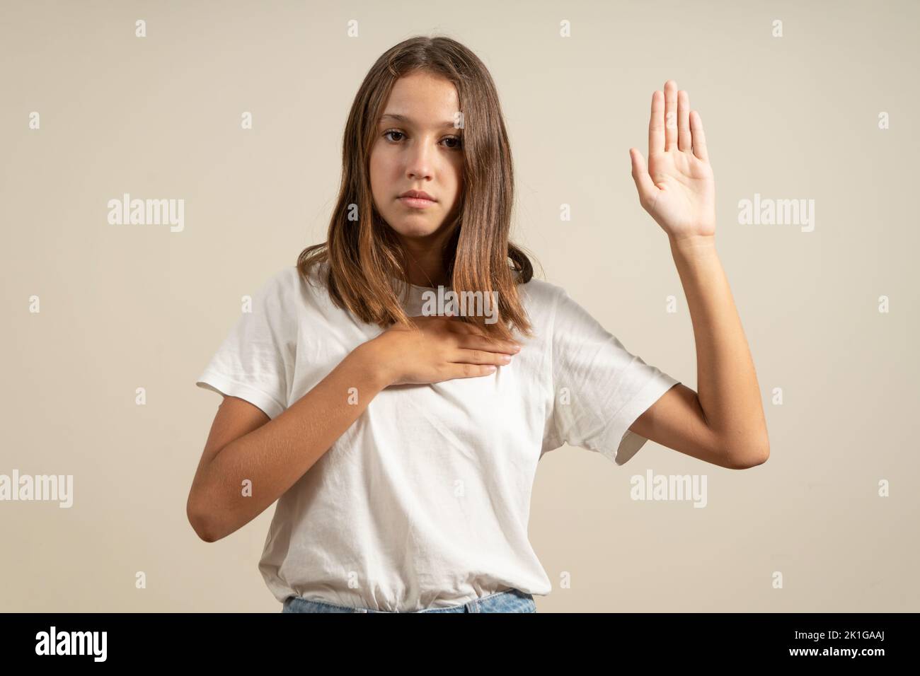 Young brunette hispanic teenager standing together over isolated beige background swearing with hand on chest and open palm, making a loyalty promise Stock Photo