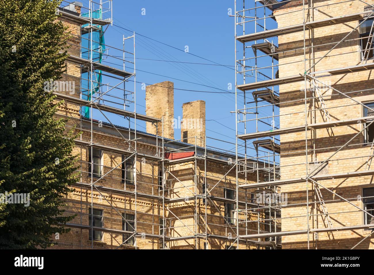 A brown brick house with metal racks and a dark green tree next to it ...