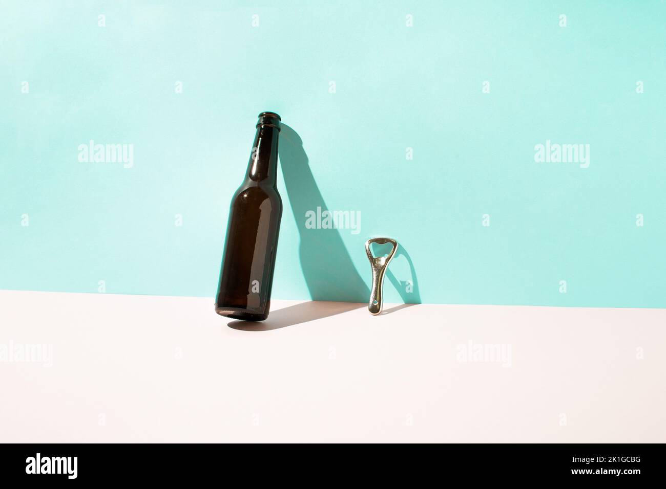 Brown beer bottle and metal bottle opener leaning against the wall with sharp shadow. Minimal summer concept. Stock Photo