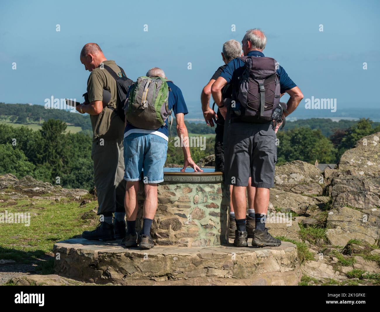 Group of adult male ramblers / walkers in shorts & walking boots with rucksacks looking at toposcope, Bradgate Park Hill, Leicestershire, England, UK Stock Photo