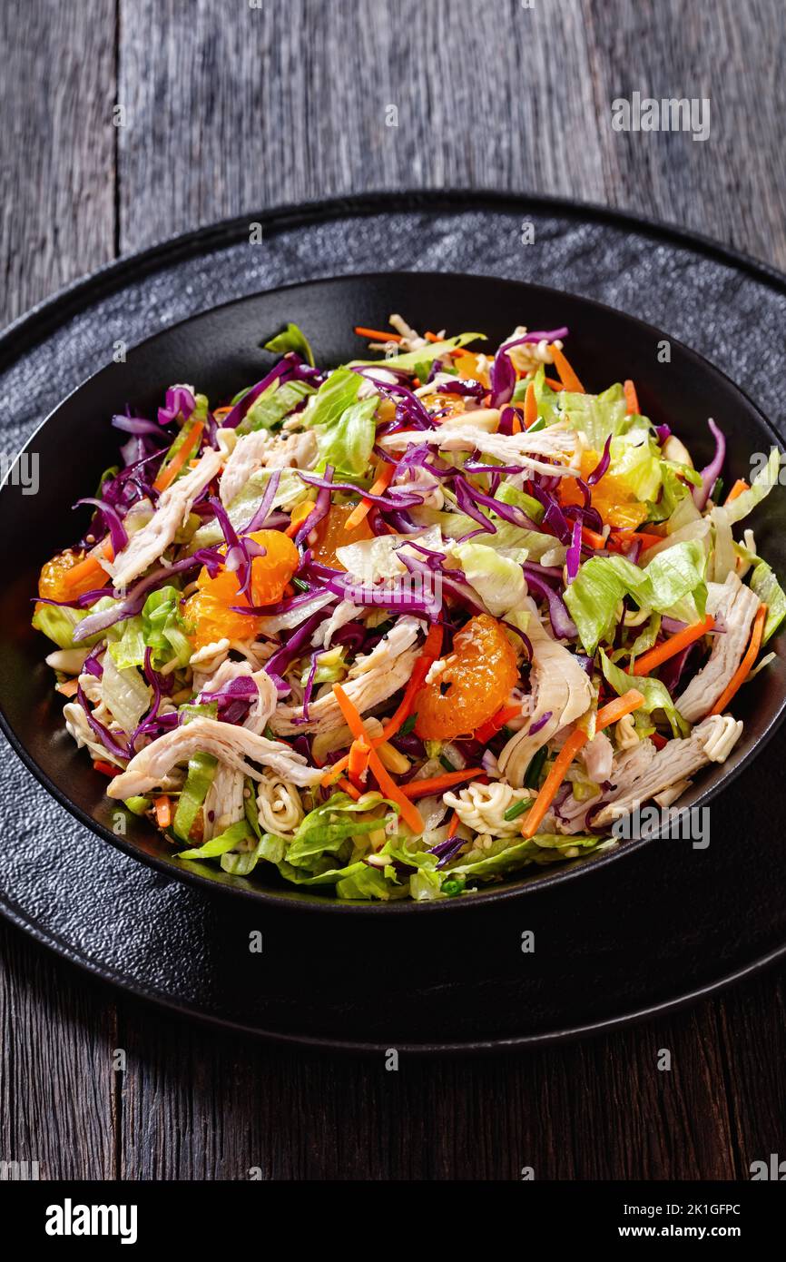 Chinese Chicken Salad with shredded chicken meat, mandarin oranges, crunchy noodles, red cabbage, napa cabbage, carrots, green onions in bowl, vertica Stock Photo