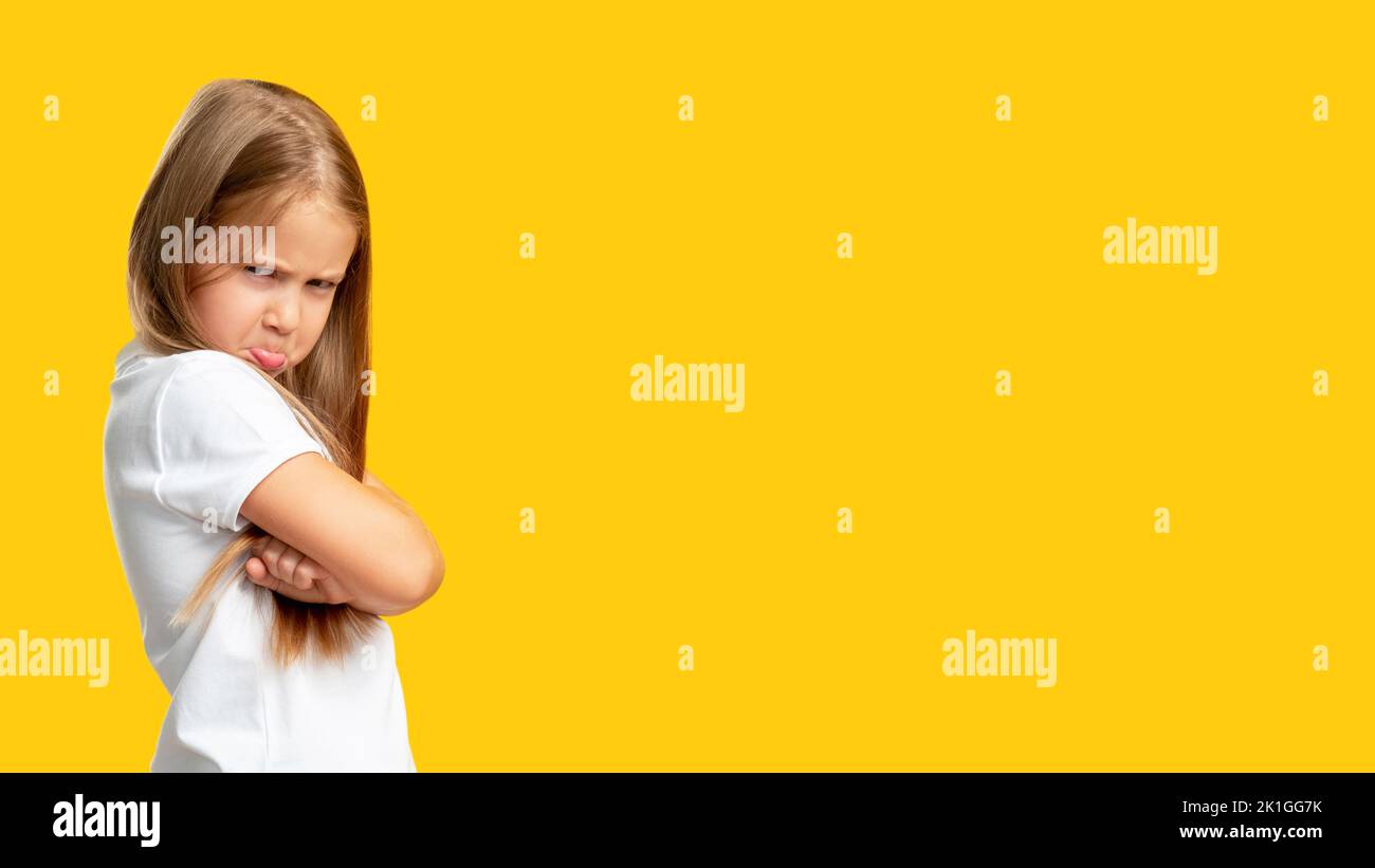 Naughty child. Disobedience problem. Discipline punishment. Portrait of angry offended little girl in white with crossed arms isolated on yellow copy Stock Photo