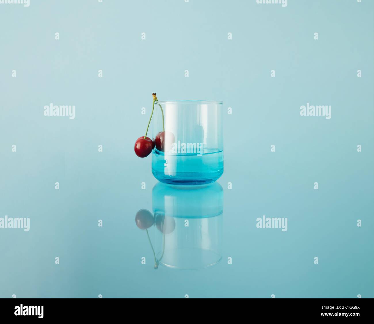 Drinking glass with fresh cherries on blue reflecting background. Mirror reflection. Stock Photo