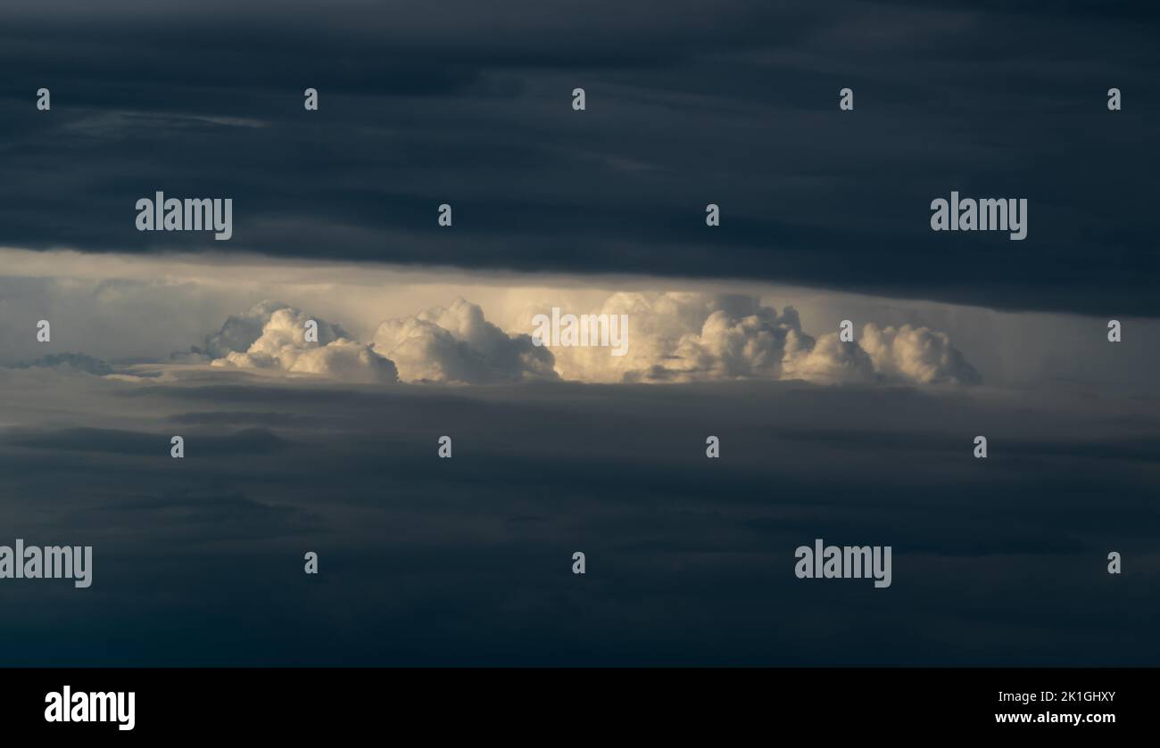 Bright sunlit cloud visible through opening in dark cloud, abstract landscape Stock Photo