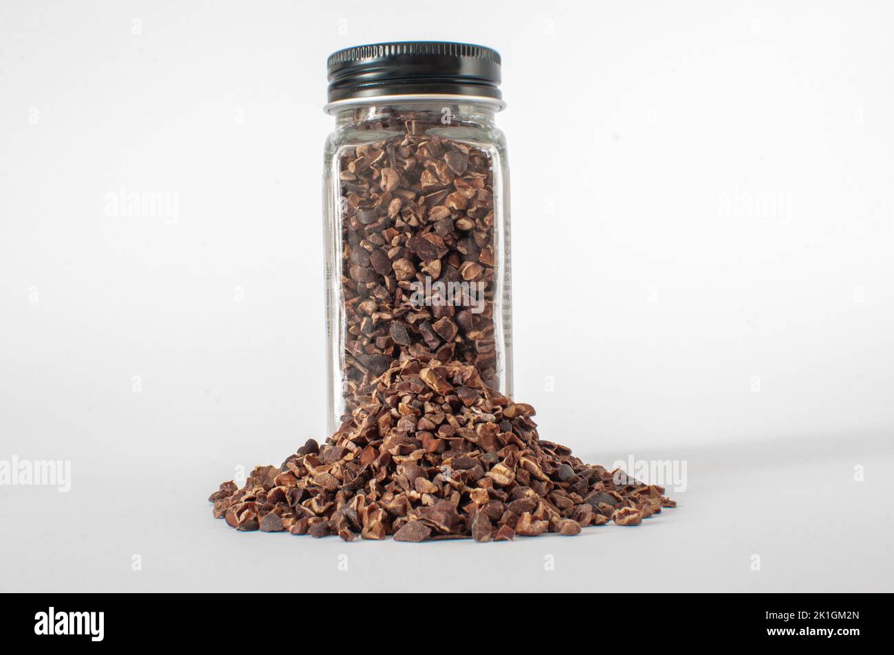 Full of organic raw cacao nibs in glass jar with black lid with a