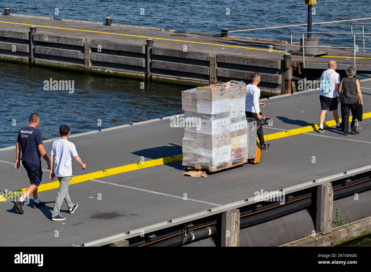 Amsterdam, Netherlands - August 2022: Crew member pulling a pallet full of supplies along a jetty for a river cruise ship moored in Amsterdam Stock Photo